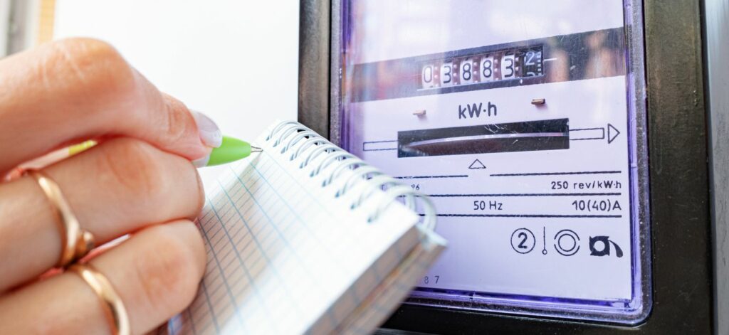 Eine Hand notiert auf einem Zettel die Zählernummer des Stromzählers vor ihr.