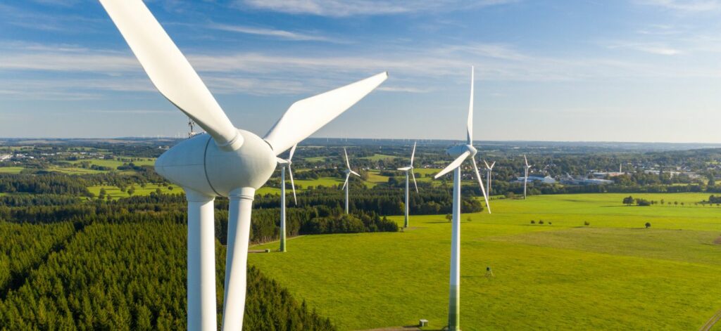 Mehrere Windräder bei schönem Wetter in landschaftlicher Umgebung.